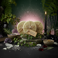 Three homegrown loofah facial discs in an enchanted apothecary setting with shimmer, ivy, herbs, gemstones, and candlelight background more shimmer with dark purple aura